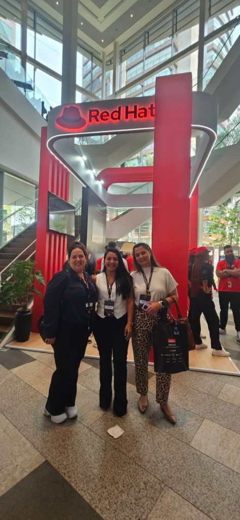 Equipe da Fast Lane presente no Red Hat Summit Connect São Paulo 2024, ao lado de banners de empresas parceiras como AWS, Microsoft e Google.